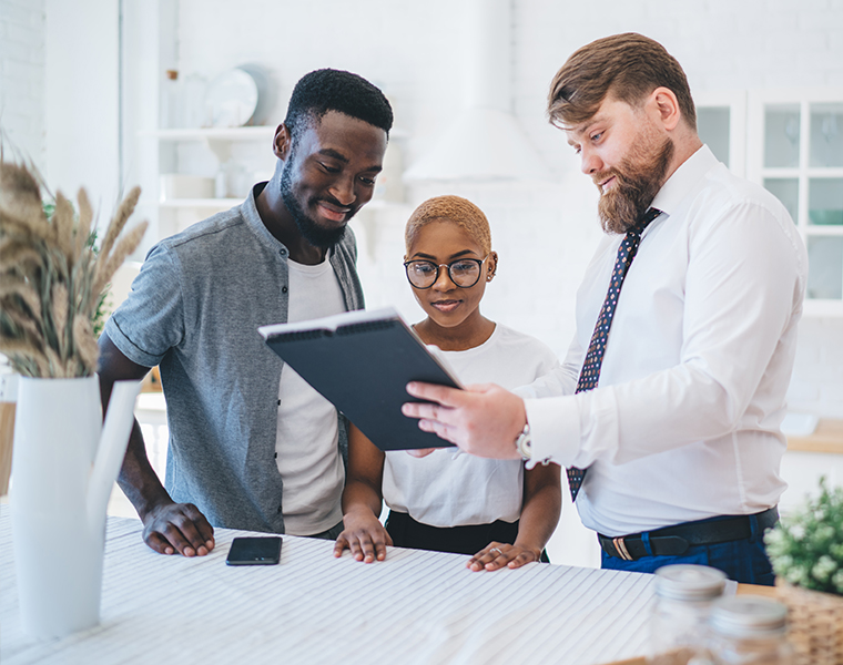 Confident agent showing documents to black couple, smiling while standing in kitchen