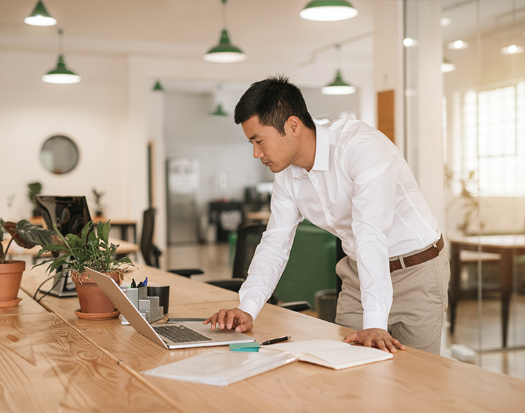 Asian businessman leaning over his desk working with a laptop